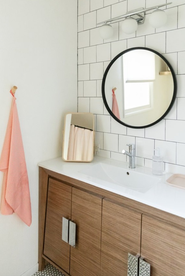 Bathroom with wood vanity, round mirror, globe vanity lights.