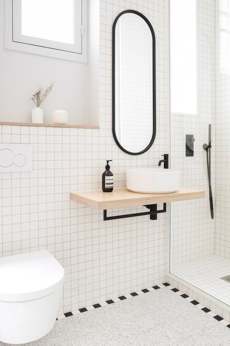 White bathroom with modern vanity, round vessel sink, black faucet, black framed oval mirror, white tile and Scandinavian Bathroom Storage Ideas.