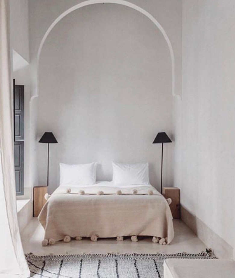 Scandinavian bedroom idea with arched detail, pair of black floor lamps, pom pom blanket