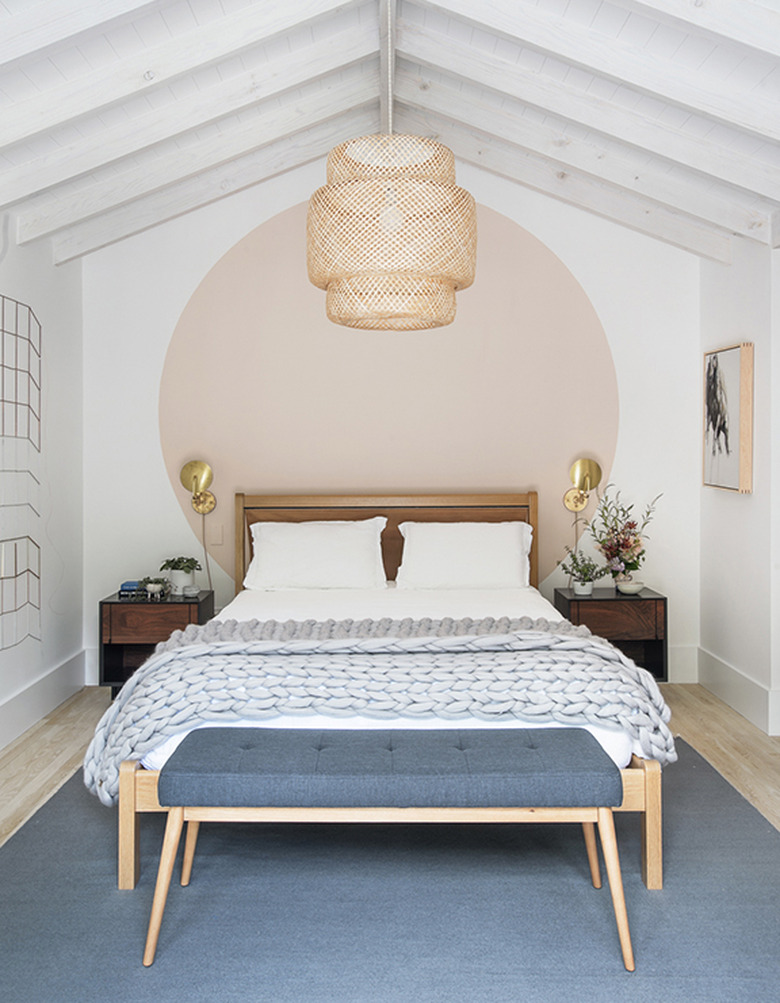 Scandinavian bedroom idea with pink circle accent wall with woven pendant above bed and a pair of sconces on wall