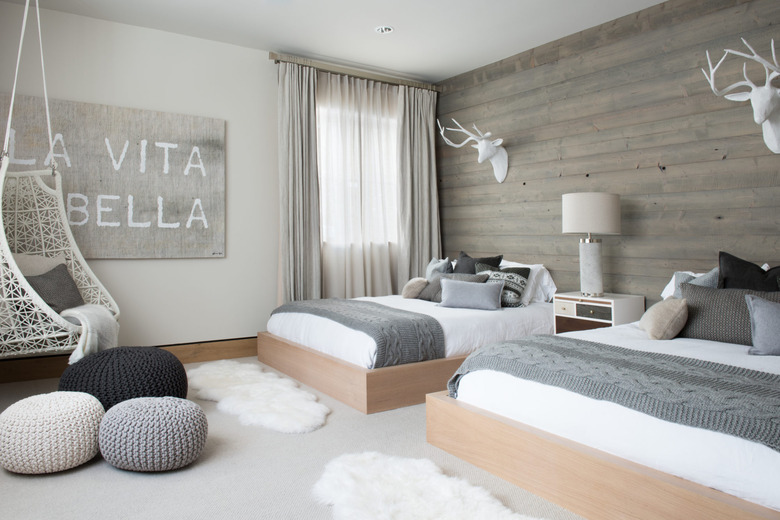 Scandinavian bedroom idea with wood feature wall in a ski cabin room with two beds and woven floor poufs and faux fur rugs