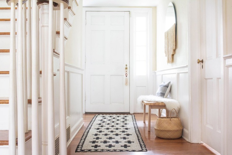 Black and white jute rug in white walled hallway with bench, basket and wood floor