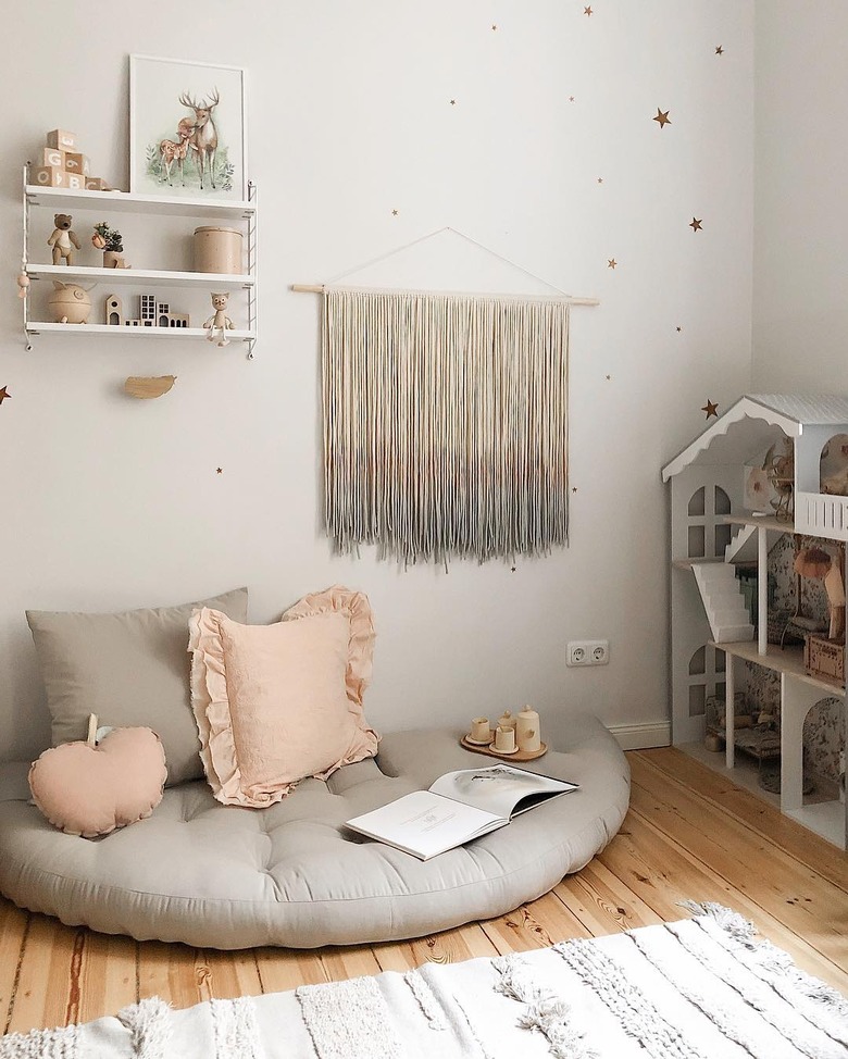 Scandinavian kids bedroom idea with gray floor cushion in kids bedroom with dollhouse and yarn wall hanging