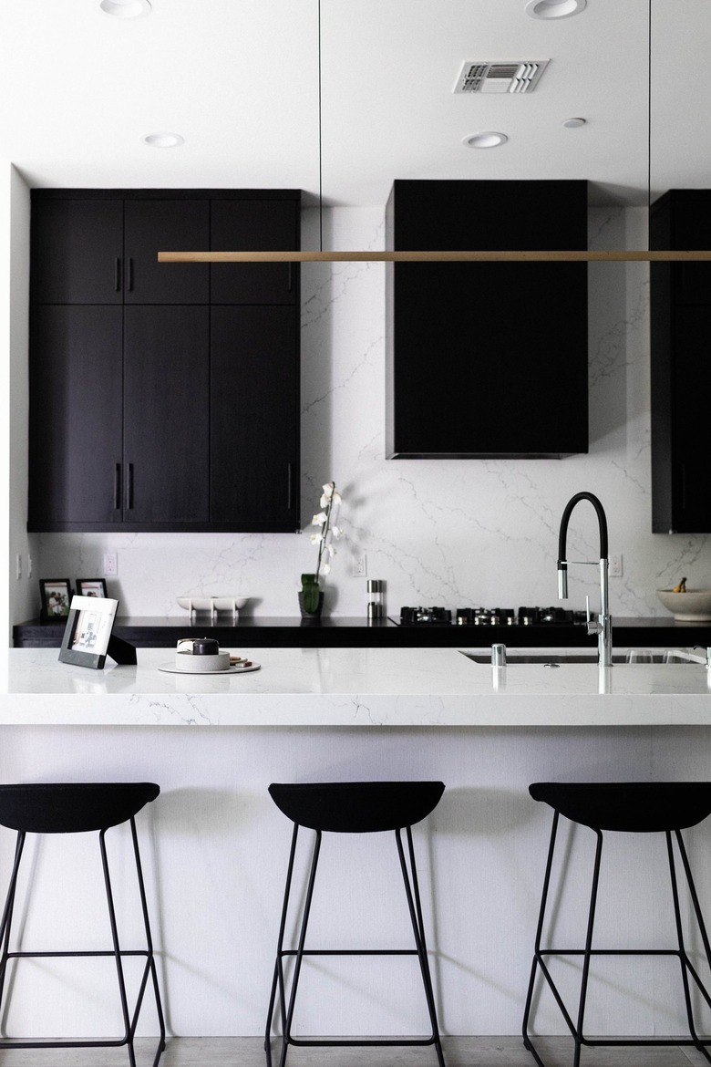 Minimalist kitchen with white counters and black cabinets and stools