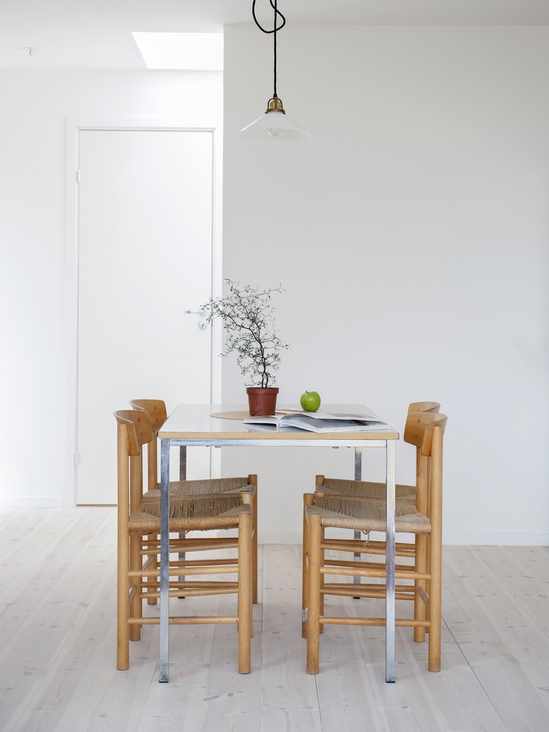 a simple wooden dining table and wooden chairs on a light wood floor in a bright white kitchen