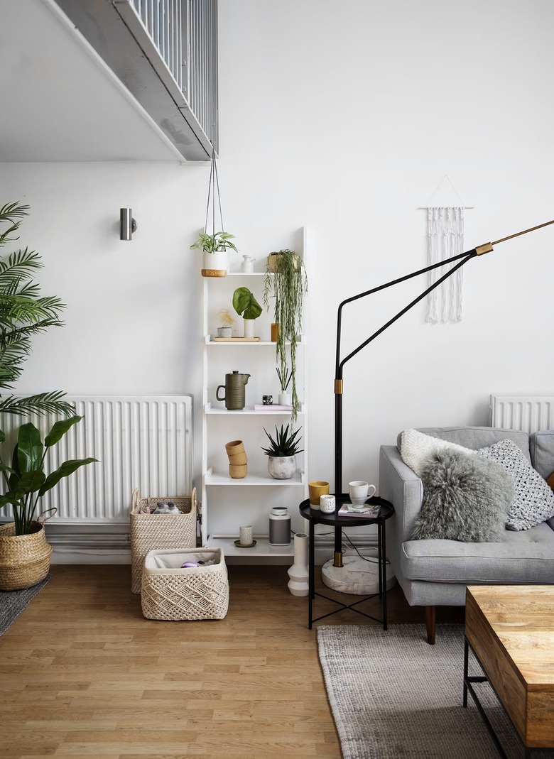 Scandinavian living room with white leaning bookcase next to floor lamp and gray sofa