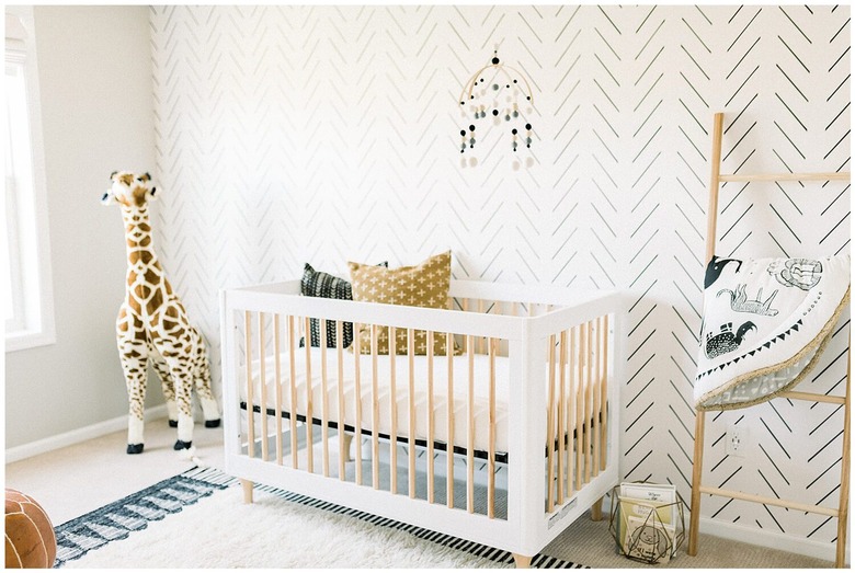 Scandinavian nursery idea with patterned wallpaper accent wall behind crib and leaning blanket rack