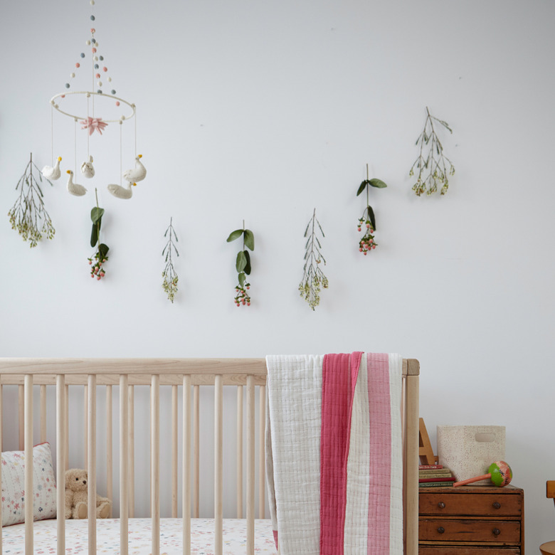 Scandinavian nursery idea with light wood crib and floral garland on wall with swan mobile hanging from ceiling