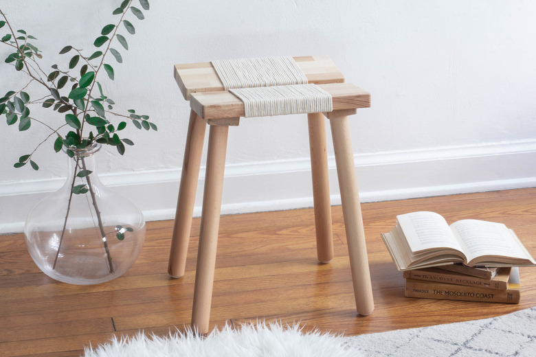 IKEA stool with rope next to greens in glass vase