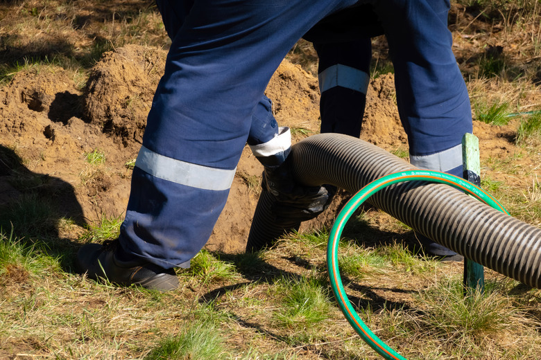 Man worker holding pipe, providing sewer cleaning service outdoor. Sewage pumping machine is unclogging blocked manhole