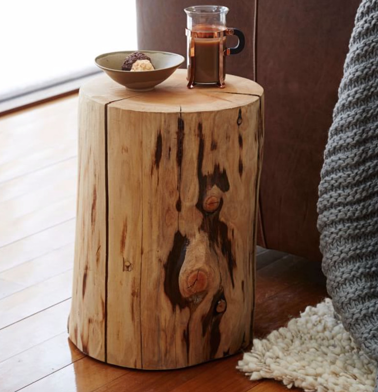 Natural tree trunk end table with tea pot, ceramic bowl, wood floors.