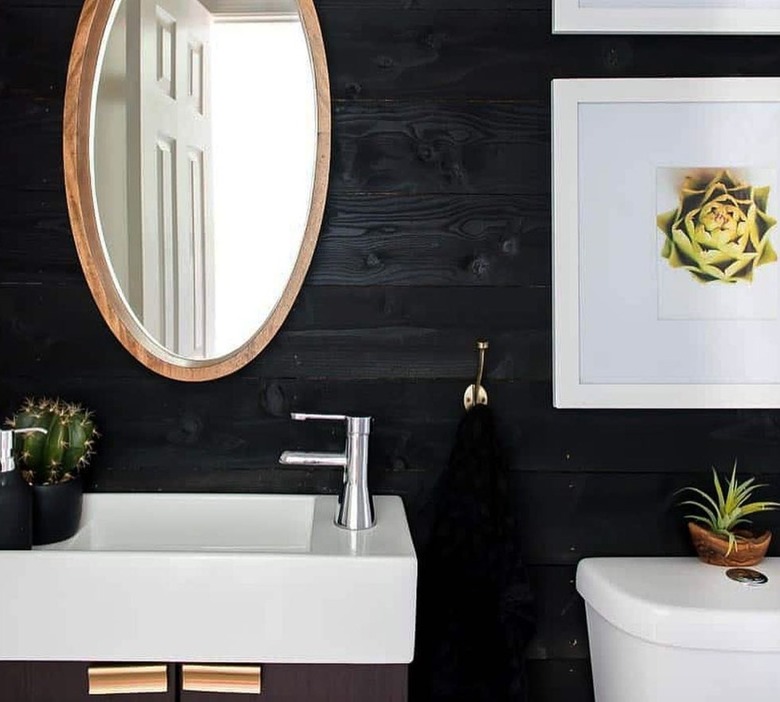 Bathroom with white sink, toilet, mirror, black shiplap walls.