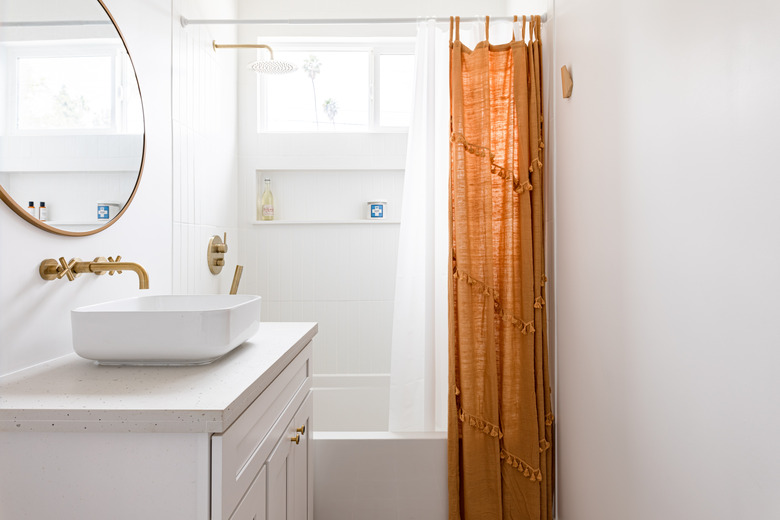 bathroom with bowl sink, circular mirror, brass fixtures and rust-orange shower curtain