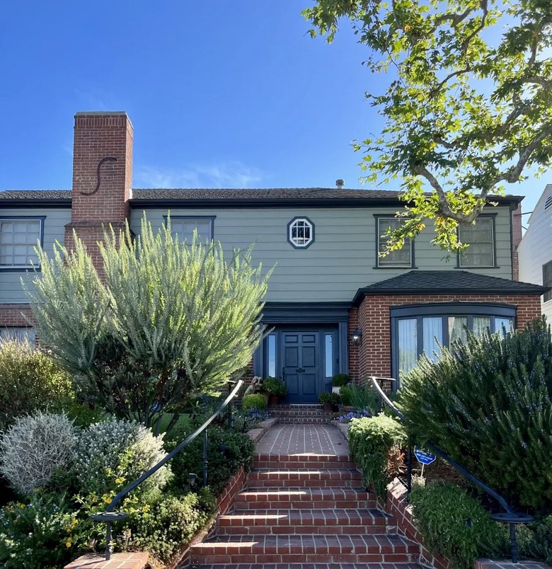 Red brick house with pale green siding and steps leading up to the entry