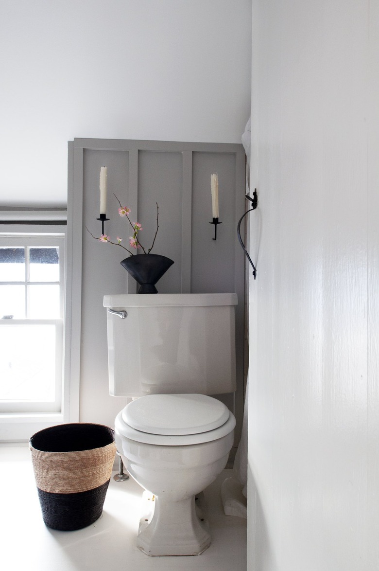 White and gray walled bathroom with candle sconces and vase with plantToilet in bathroom.