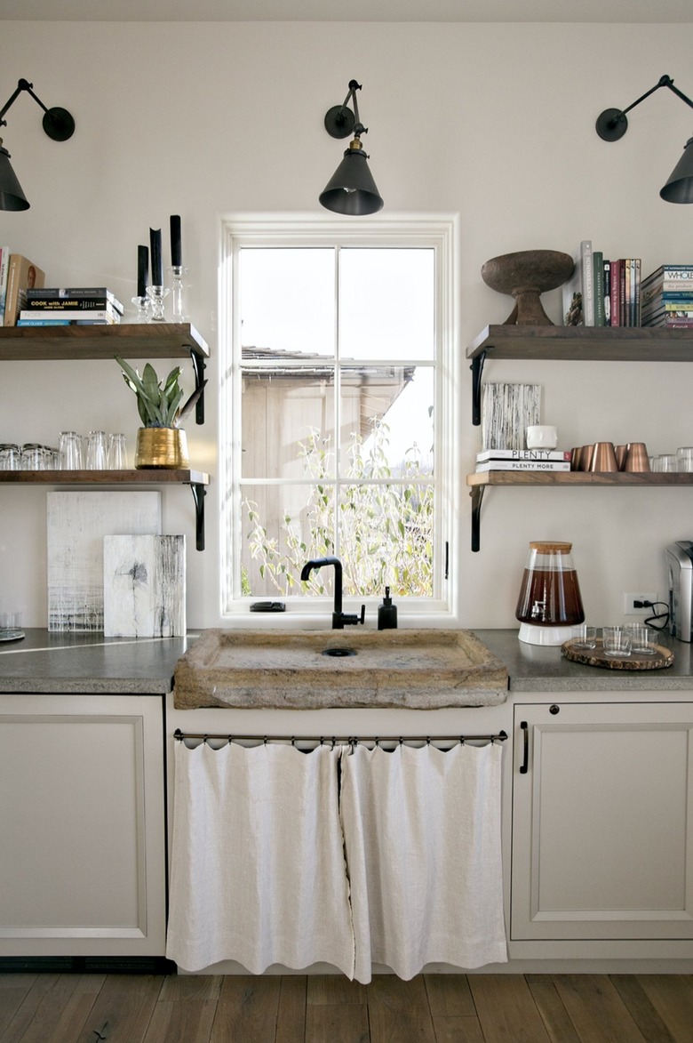 White and black kitchen with white curtains instead of cabinet doors under sink.