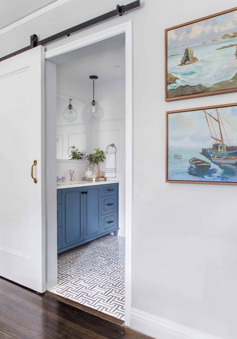 White sliding small bathroom door with blue vanity cabinet and patterned floor tile