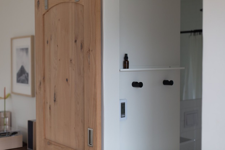 Bathroom view from hallway with wooden door and shelf with towel hooks beneath