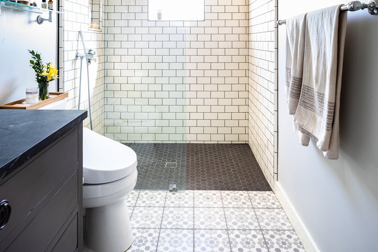 A white tiled bathroom with a glass door shower and black-gray accents