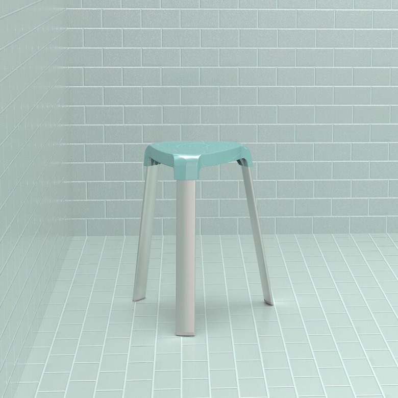 A three-legged alumnium stool with a light blue seat and grey legs sits in a corner with rectangular light blue tile.