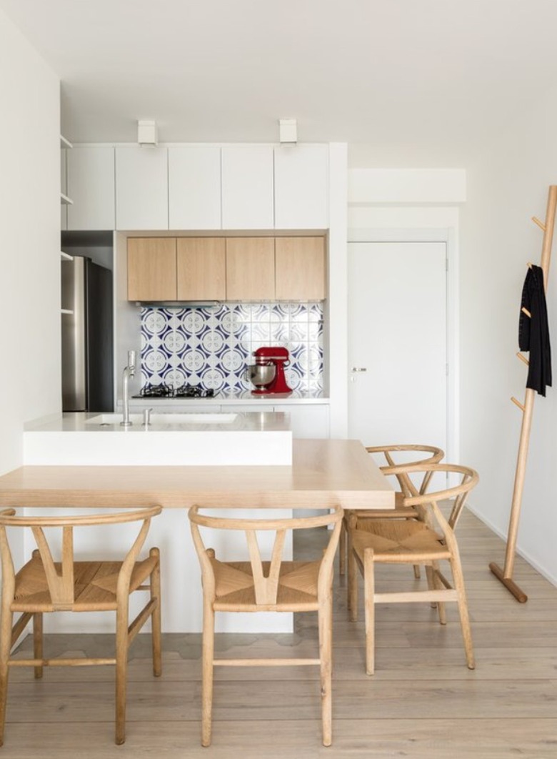 Small kitchen with dining counter, tile backsplash, modern wood chairs.