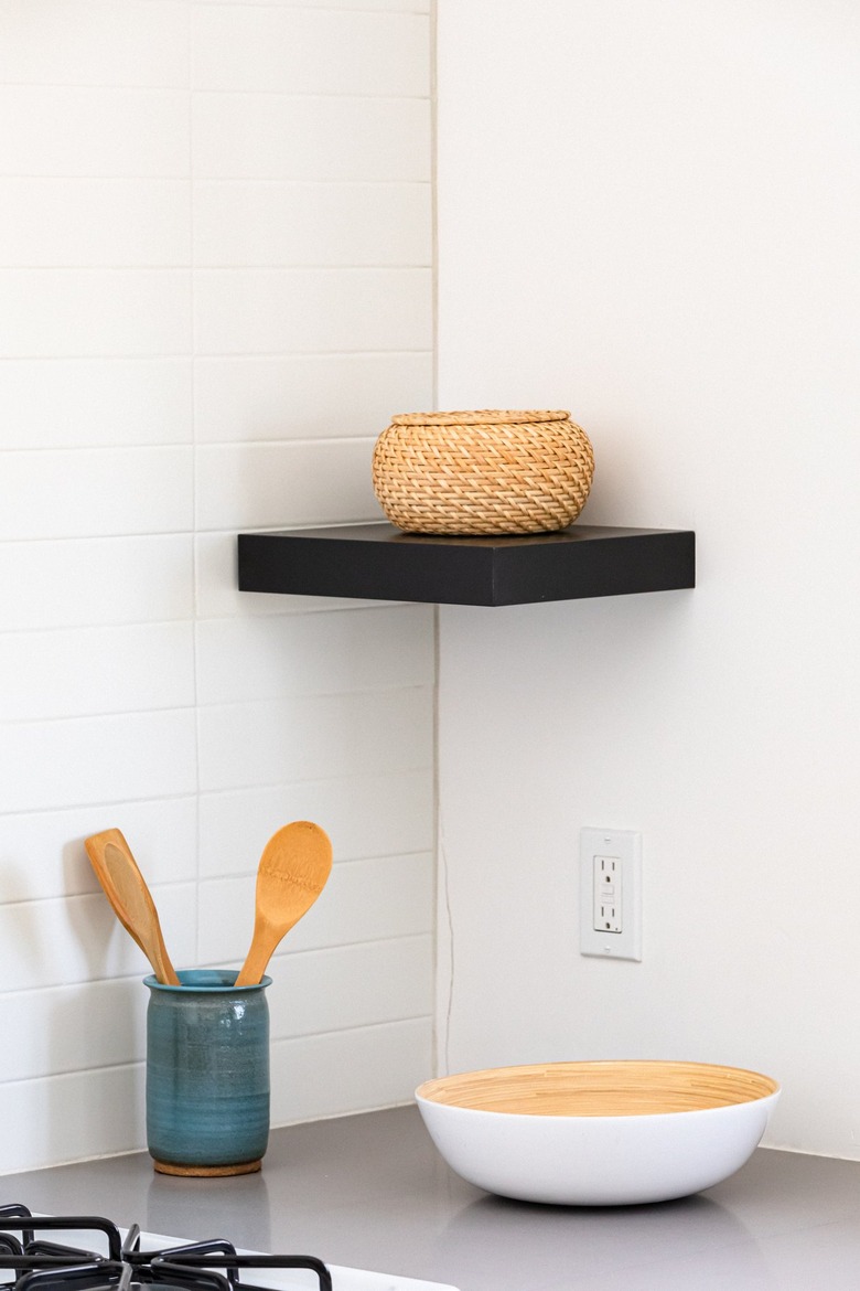 Black shelf with a wicker bowl and a gray kitchen countertop with dishware