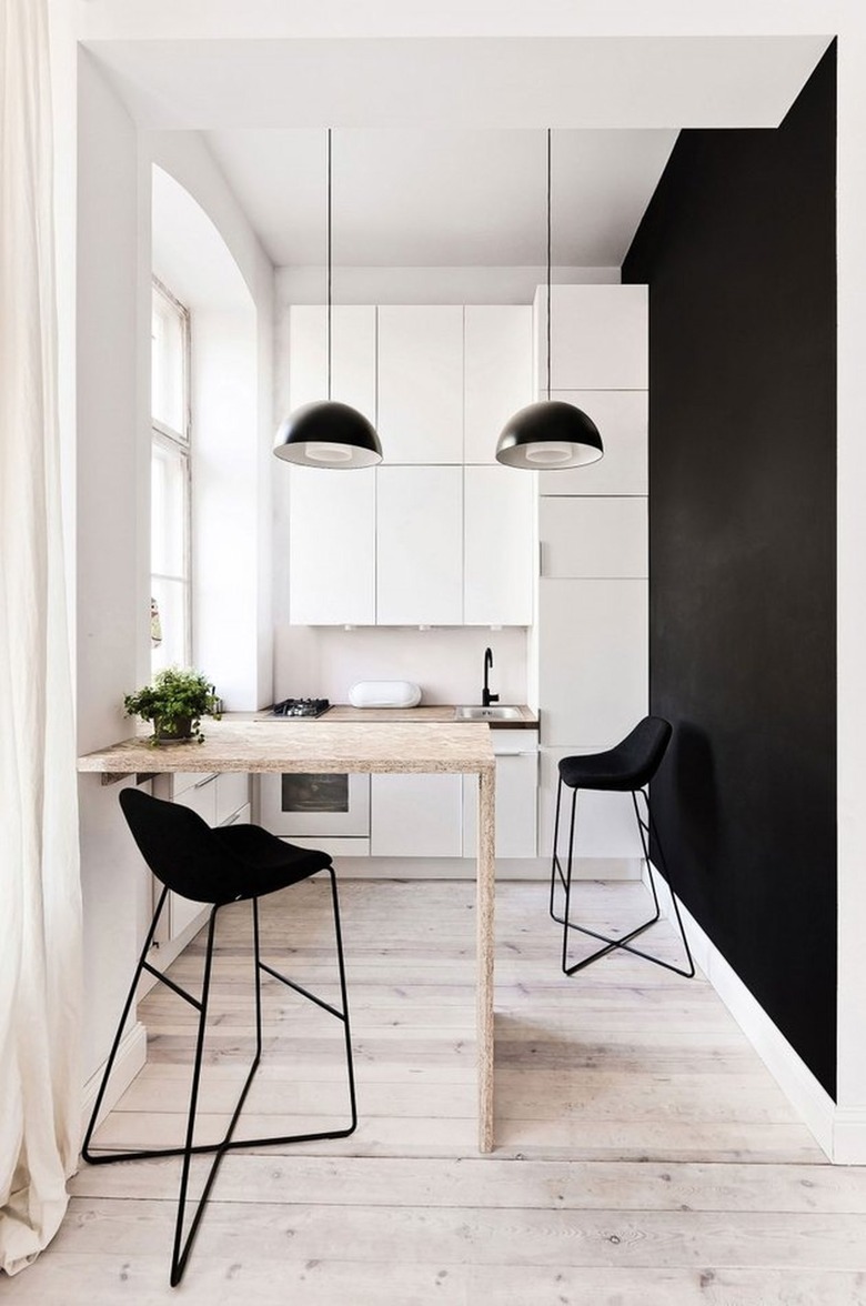 Small kitchen with black accent wall, small bar, white cabinets.