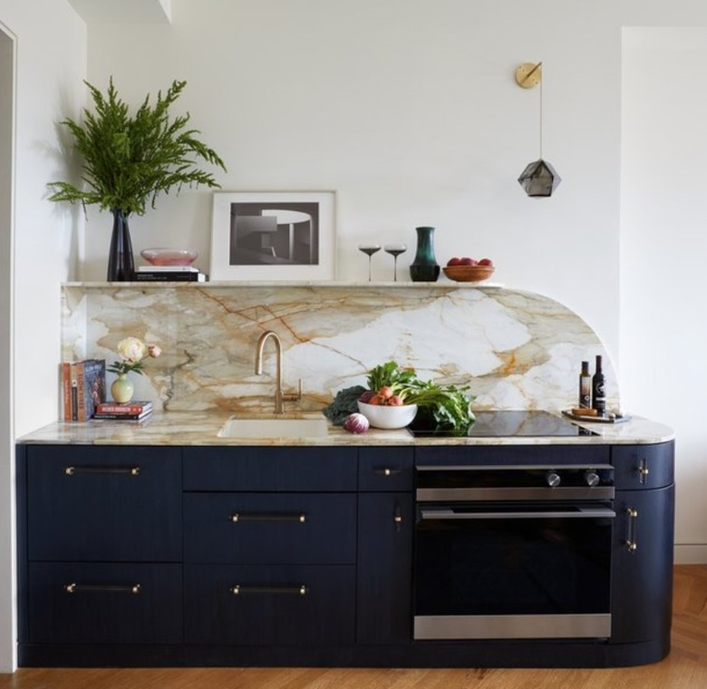 Art deco kitchen with navy cabinets, marble counter and backsplash, plant, art.