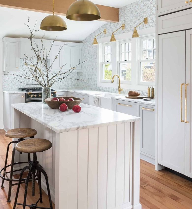 Modern farmhouse kitchen with island, marble, brass pendants, sconces, wood floor.