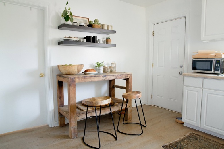 White cabinets and wood floor kitchen, wood stools at a wood side table, black shelves with dish ware.