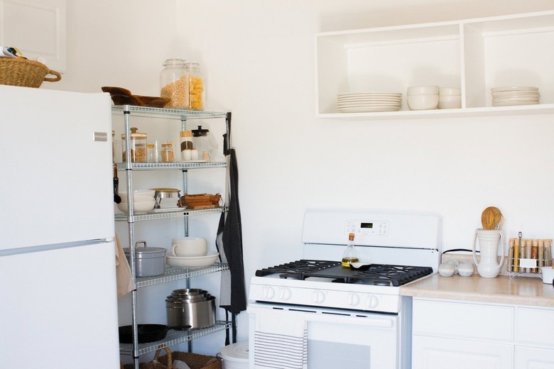 Kitchen with metal racks of dish ware and containers of dry goods, stove, white cabinets and beige counters, white dishes