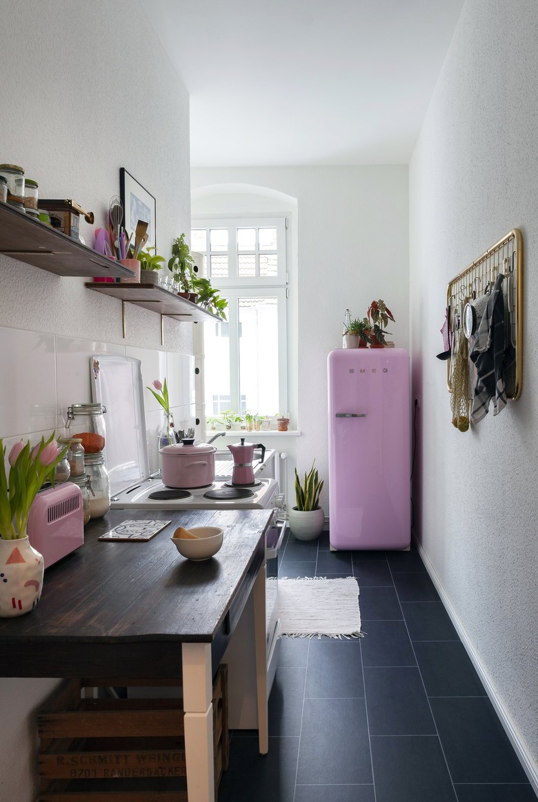 small narrow kitchen with black tile floors and pink smeg fridge