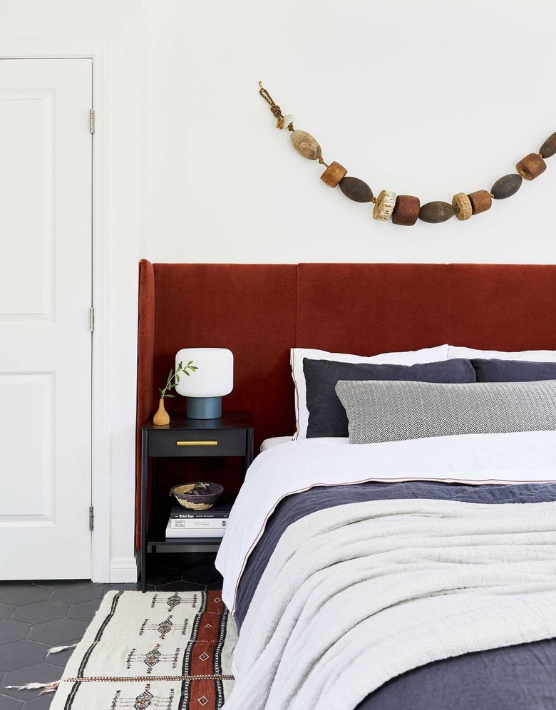 small bedroom with red velvet headboard and vintage buoy wall art