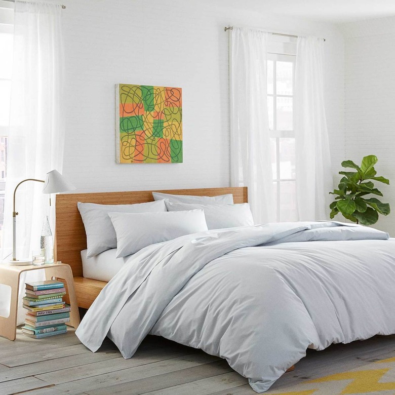 bedroom with side table with white lamp, bed with white sheets, and colorful artwork above the bed