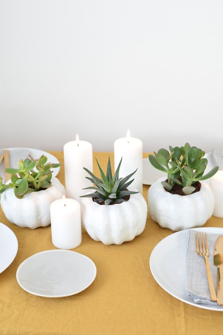 all-white pumpkin planters with white candles on a tabletop with place settings