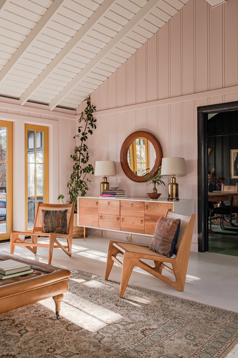 A-frame living room with pink walls, earthy furniture, yellow French doors, and midcentury accents.