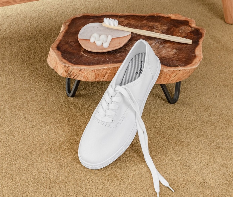 Cleaning a white tennis shoe with toothpaste; a white shoe is next to a wooden stool that contains a plate of toothpaste