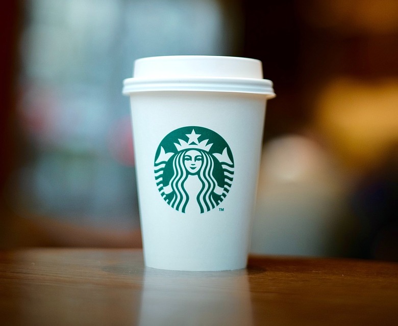 White Starbucks hot cup with the logo on a wooden surface with a blurred background.