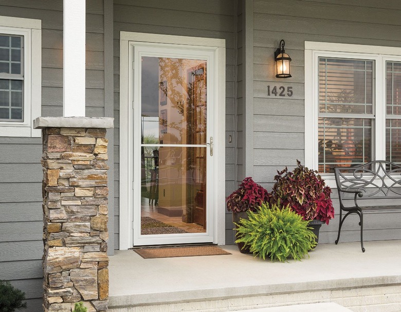 A glass storm door on a house with gray-green siding