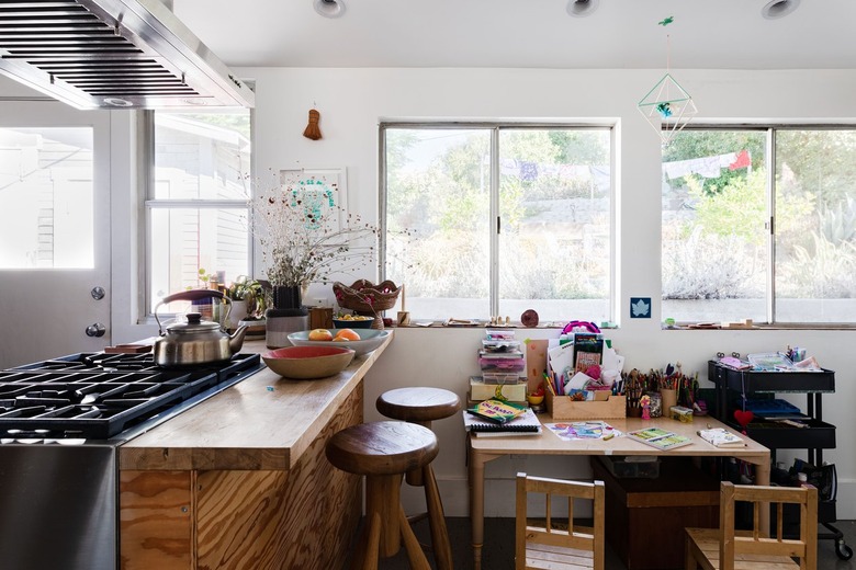 A kitchen with wood countertops, stove vent, stools and a kid's art desk