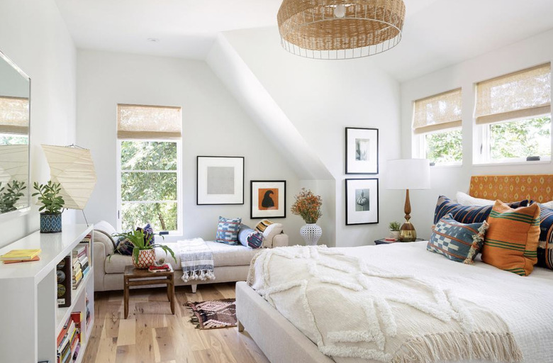 studio bedroom idea for bright and airy second-floor bedroom with white bedding, a white shelf, and a beige chaise lounge in the window