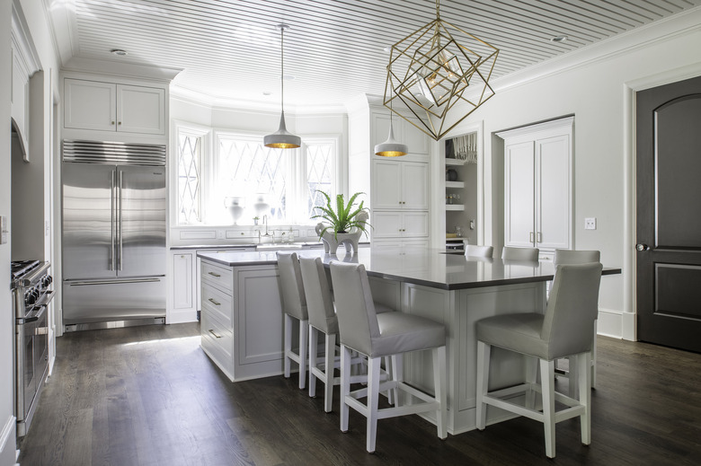 White T-shaped kitchen island with upholstered chairs, pendant lights, and geometric chandelier