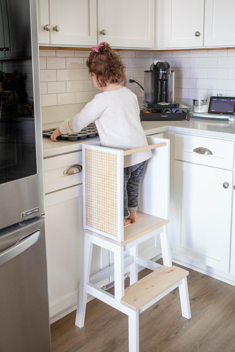 Young girl on a step stool in a white kitchen preparing to bake