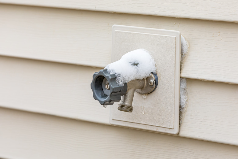 Outdoor hose bib or water spigot covered in snow during winter. Home repair, maintenance and weatherproofing concept.