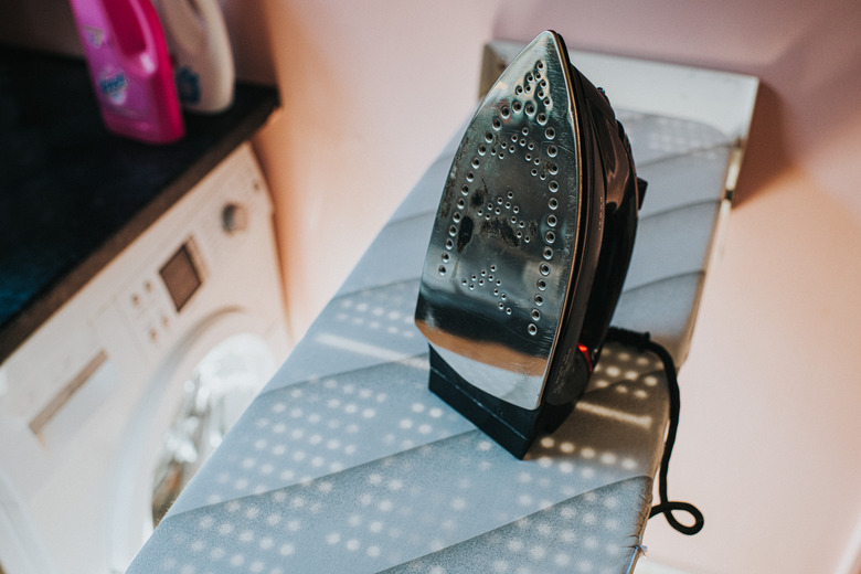 An iron sitting upright on an ironing board.