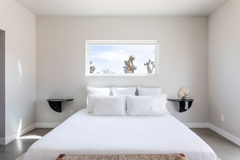 Minimalist bedroom with double black nightstand shelves, white bedding, and a desert window view.