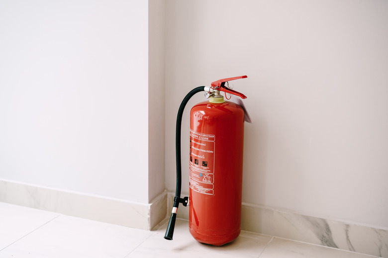 A close-up of a red fire extinguisher on the floor in the corner against a white wall.