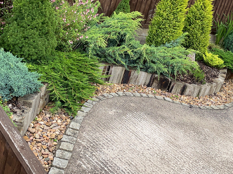 Curved concrete driveway bordered by pavers, gravel mulch and raised-bed timber-blocked edge planted with dwarf conifers.