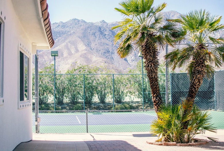 Outdoor tennis pavilion with cluster of palm trees, white-walled villa, and tennis courts against mountains