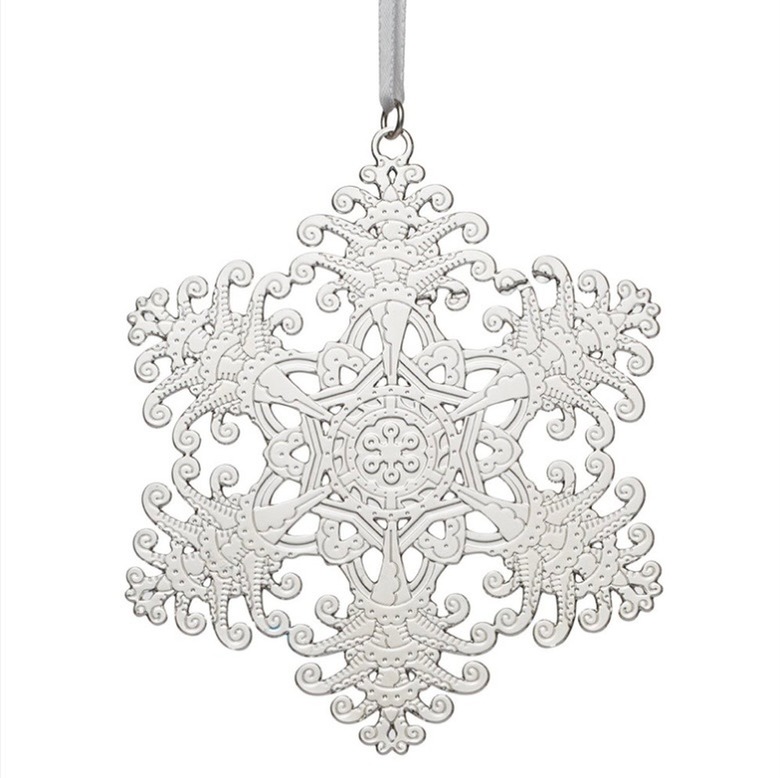 An ornate silver snowflake Christmas tree ornament, featuring intricate swirls and texture, it hangs on a silver chord.